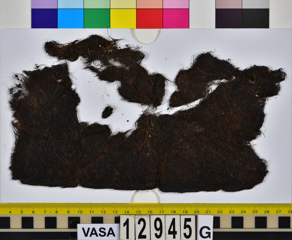 Textilfragment.
15 textilfragment uppdelade på fyndnummer 12945a-g.
Fnr 12945a består av fyra fragment av ull vävda i tuskaft. Två av fragmenten har rester av söm eller fåll samt har varit valkade.
Fnr 12945b består av två fragment av ull vävda i tuskaft. 
Fnr 12945c består av ett fragment av ull vävt i tuskaft. Fragmentet kan ha varit valkat på ena sidan.
Fnr 12945d består av ett fragment av ull vävt i tuskaft. Fragmentet har en söm med rester av stygn kvar i ena kanten.
Fnr 12945e består av tre fragment av ull vävda i tuskaft. Fragmentet har en tydlig originalkant bevarad.
Fnr 12945f består av ett filtat fragment. Kan möjligen ha varit en del av ett hattbrätte.
Fnr 12945g består av tre filtade fragment, troligen av ull.