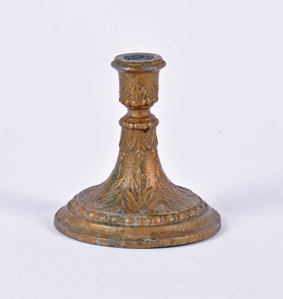 Lysestake i støpt metall. Overflaten har bladmotiv og border. Dekket med messingfarget maling, delvis avslitt.