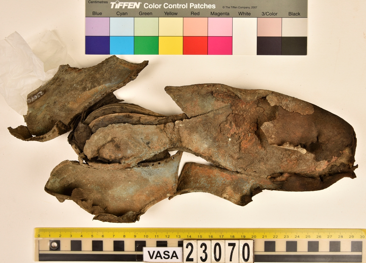 Sko.
Inuti skorna hittades även fragment från olika textilier som ursprungligen varit ett par strumpor. Idag sitter ett stickat fragment av ull fast i vänsterskon (23070) med avigsidan uppåt. I fyndet finns även en mängd lösa stickade fragment som idag är mycket korroderade och vissa helt mineraliserade av järn vilket har gjort textilen stenhård och därmed oerhört skör (23070a-c). Utifrån minskningar som några små fragment har så har det varit möjligt att rekonstruera strumpans tå. Genom att pussla ihop fragmenten som ursprungligen har suttit ihop har det på så vis gått att avgöra hur strumpans tå har varit konstruerad. Då textilen är så fragmentarisk är det inte möjligt att avgöra hur resten av strumpan har sett ut eller varit konstruerad. Däremot så finns det fragment av ett kypertvävt tyg av ull som på vissa ställen ligger dubbelt med det stickade 23070c). Ett av dessa fragment har stelnat i formen så som den suttit på fotens främre del inuti skon. Detta fragment täcker delvis det stickade tyget och har dessutom spår av kaststygn längs en kant. Så som det vävda tyget är placerat på det stickade tyget pekar på att man använt det som lagningslappar till sina stickade strumpor. 
I fyndet finns det även korroderade järnklumpar, ett tuskaftsvävt tyg av ull och rester av ett grovt bastfibergarn och två mindre läderfragment (23070d-f). Det är möjligt att även dessa har tillhört strumpan och/eller skon.

För mer detaljerad information från textildokumentationen (år 2022) se länkade filer.

Skodokumentation 2022:
Ovanläder. Tillverkad i getskinn av god kvalitet. Hör ihop med fyndnummer 23069 (Yngves skor). Tillverkades på en rak läst och bars på vänster fot. Inga dekorationer Det finns stygnhål som visar att det funnits invändiga förstärkningar (men förstärkningslappen saknas). Det finns delaminering men inga lagningar.
För mer information, se Länkade filer: Uppritning

Text in english:
This is the upper of a shoe of more “extreme fashion”, made of goatskin leather of good quality, probably made on a straight last and worn of the left foot, with no decorative features. The upper couples with 23069, together composing Yngve’s shoes. There are internal reinforcements missing from the upper and delamination, there are no repairs.
For more information, go to Länkade filer: Uppritning