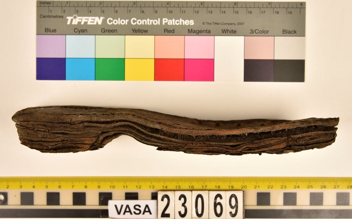 Dokumentation 1996:
Delar och fragment av sko: en skobotten samt ett fragmentariskt ovanläder, tre bitar av ett filtliknande material, ett 15-tal fragment av bottenläder samt sex mindre fragment av trä.
Skobottnen har kvarsittande tråd och träpligg. Yttersulan är ritsad. Klacken består av fem klacklappar som är placerade mellan ytter- och innersulan. Innersulans läder är mycket kraftigt, ca 6 mm tjock. Ovanlädret är sprött och fragmentariskt samt har blå och rostfärgade utfällningar.

Text in English: 
Various parts and fragments of a shoe, consisting of a sole with fragments of vamp (upper leather), three pieces of a felt-like material, some 15 fragments of sole or bottom leather and six smaller fragments of wood.
There are remains of thread and wooden pegs on the shoe sole. The outsole is channeled. The heel is made up of five heel lifts placed between the insole and outsole. The leather of the insole is very thick, ca 6 mm. The upper leather is fragile and fragmentary, and has blue and rust-coloured precipitations.

Dokumentation 2022:
Skobotten och delar av ovanläder till en öppen randsko. Tillverkade i getskinn av god kvalitet. Skapades på en rak läst och bars på höger fot. Klacken som är lagad med en läderlapp under sulan. Inga dekorationer. Det finns tecken på delaminering. Fragment från en stickad strumpa hittades inuti skon. Det finns lagningar med träpligg på sulan och hälen. Skobotten hör ihop med fyndnummer 23070.
För mer information, se Länkade filer: Uppritning

Text in english:
This is the bottom unit and upper fragments of an open shoe, made of goatskin leather of good quality, of randed construction with a patch heel, made on a straight last and worn on the right foot, with no decorative features. The bottom unit pairs with 23070. There are signs of delamination and fragments of a knitted stocking were found inside the shoe. There are pegged repairs to sole and heel.
For more information, go to Länkade filer: Uppritning
