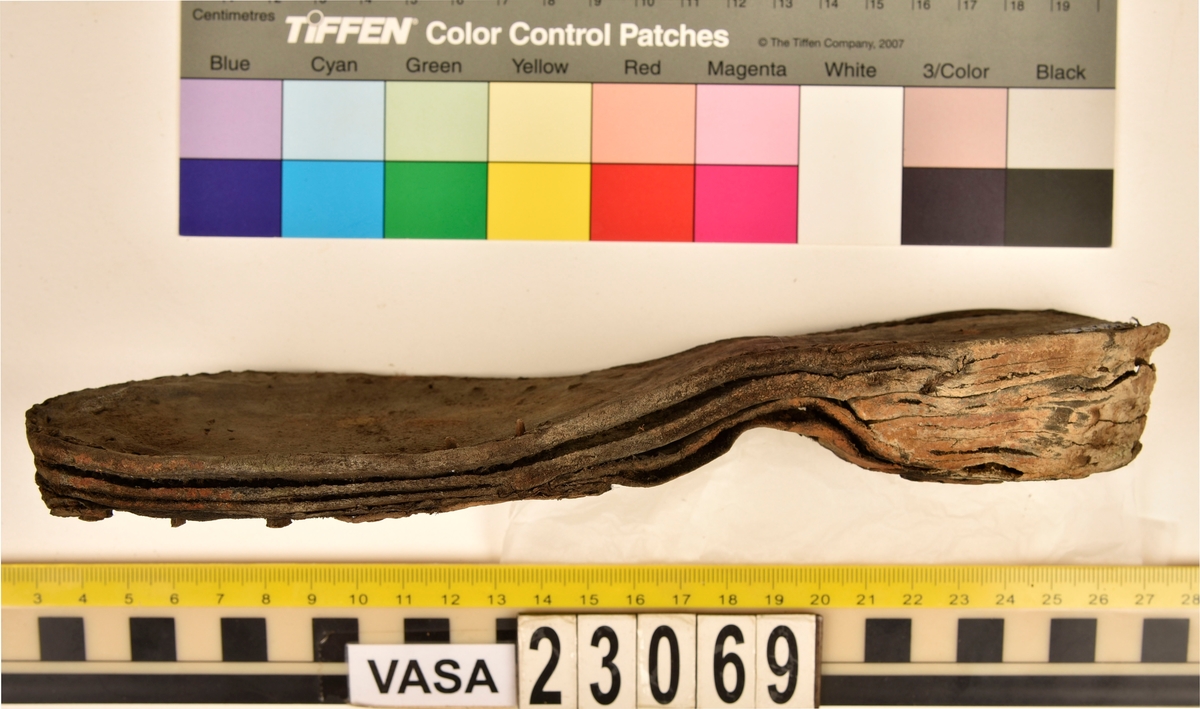 Dokumentation 1996:
Delar och fragment av sko: en skobotten samt ett fragmentariskt ovanläder, tre bitar av ett filtliknande material, ett 15-tal fragment av bottenläder samt sex mindre fragment av trä.
Skobottnen har kvarsittande tråd och träpligg. Yttersulan är ritsad. Klacken består av fem klacklappar som är placerade mellan ytter- och innersulan. Innersulans läder är mycket kraftigt, ca 6 mm tjock. Ovanlädret är sprött och fragmentariskt samt har blå och rostfärgade utfällningar.

Text in English: 
Various parts and fragments of a shoe, consisting of a sole with fragments of vamp (upper leather), three pieces of a felt-like material, some 15 fragments of sole or bottom leather and six smaller fragments of wood.
There are remains of thread and wooden pegs on the shoe sole. The outsole is channeled. The heel is made up of five heel lifts placed between the insole and outsole. The leather of the insole is very thick, ca 6 mm. The upper leather is fragile and fragmentary, and has blue and rust-coloured precipitations.

Dokumentation 2022:
Skobotten och delar av ovanläder till en öppen randsko. Tillverkade i getskinn av god kvalitet. Skapades på en rak läst och bars på höger fot. Klacken som är lagad med en läderlapp under sulan. Inga dekorationer. Det finns tecken på delaminering. Fragment från en stickad strumpa hittades inuti skon. Det finns lagningar med träpligg på sulan och hälen. Skobotten hör ihop med fyndnummer 23070.
För mer information, se Länkade filer: Uppritning

Text in english:
This is the bottom unit and upper fragments of an open shoe, made of goatskin leather of good quality, of randed construction with a patch heel, made on a straight last and worn on the right foot, with no decorative features. The bottom unit pairs with 23070. There are signs of delamination and fragments of a knitted stocking were found inside the shoe. There are pegged repairs to sole and heel.
For more information, go to Länkade filer: Uppritning
