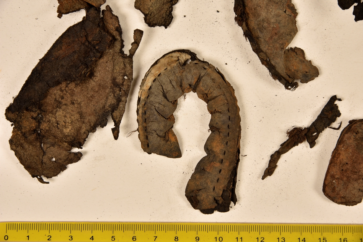 Dokumentation 1996:
Delar och fragment av sko: en skobotten samt ett fragmentariskt ovanläder, tre bitar av ett filtliknande material, ett 15-tal fragment av bottenläder samt sex mindre fragment av trä.
Skobottnen har kvarsittande tråd och träpligg. Yttersulan är ritsad. Klacken består av fem klacklappar som är placerade mellan ytter- och innersulan. Innersulans läder är mycket kraftigt, ca 6 mm tjock. Ovanlädret är sprött och fragmentariskt samt har blå och rostfärgade utfällningar.

Text in English: 
Various parts and fragments of a shoe, consisting of a sole with fragments of vamp (upper leather), three pieces of a felt-like material, some 15 fragments of sole or bottom leather and six smaller fragments of wood.
There are remains of thread and wooden pegs on the shoe sole. The outsole is channeled. The heel is made up of five heel lifts placed between the insole and outsole. The leather of the insole is very thick, ca 6 mm. The upper leather is fragile and fragmentary, and has blue and rust-coloured precipitations.

Dokumentation 2022:
Skobotten och delar av ovanläder till en öppen randsko. Tillverkade i getskinn av god kvalitet. Skapades på en rak läst och bars på höger fot. Klacken som är lagad med en läderlapp under sulan. Inga dekorationer. Det finns tecken på delaminering. Fragment från en stickad strumpa hittades inuti skon. Det finns lagningar med träpligg på sulan och hälen. Skobotten hör ihop med fyndnummer 23070.
För mer information, se Länkade filer: Uppritning

Text in english:
This is the bottom unit and upper fragments of an open shoe, made of goatskin leather of good quality, of randed construction with a patch heel, made on a straight last and worn on the right foot, with no decorative features. The bottom unit pairs with 23070. There are signs of delamination and fragments of a knitted stocking were found inside the shoe. There are pegged repairs to sole and heel.
For more information, go to Länkade filer: Uppritning