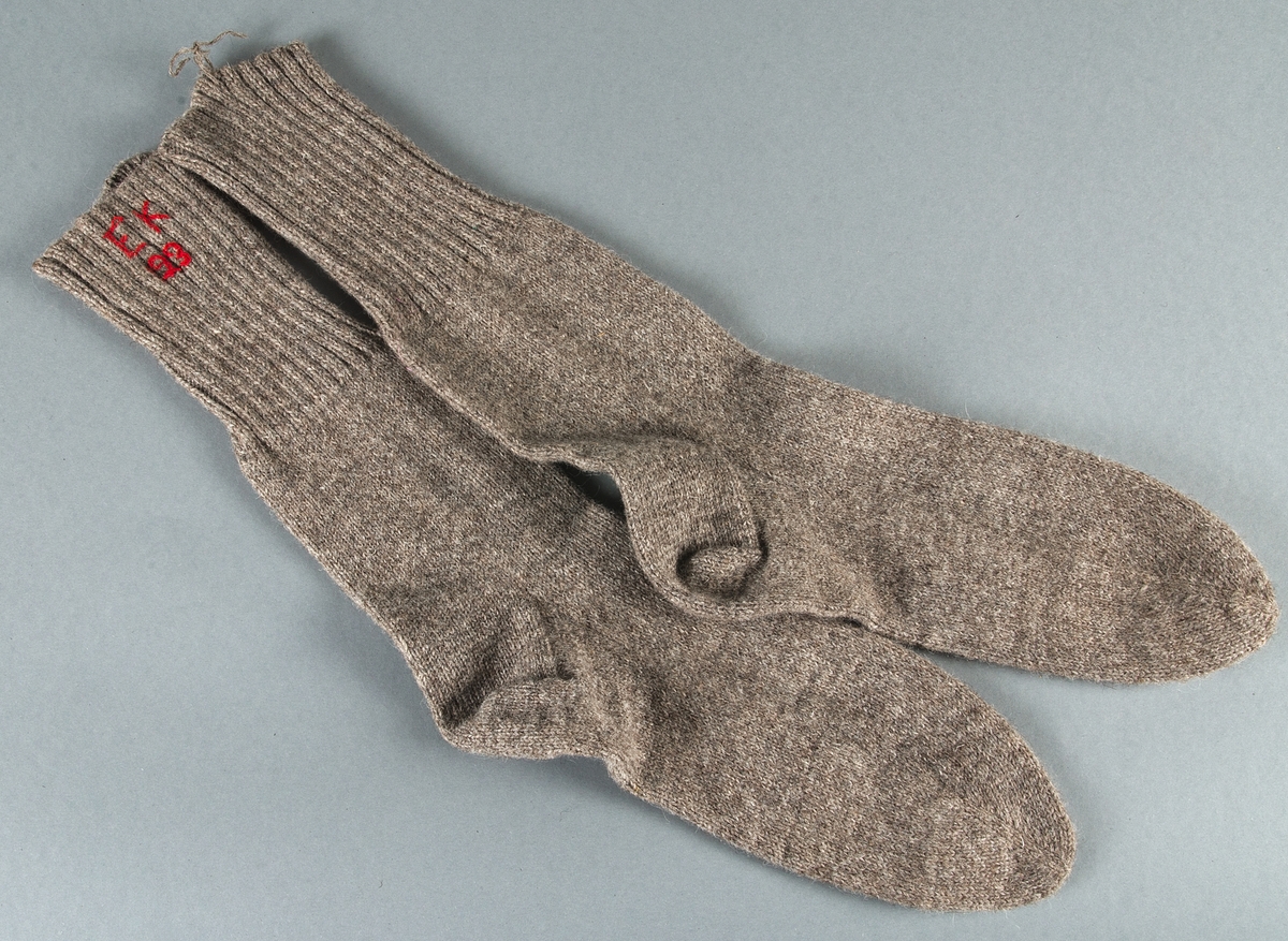 Två par stickade yllesockor. Långa skaft. Det ena paret sitter ihop med lila/vitt paketsnöre. Ett par ljust brungrå och ett med med ljust brungrå skaft och ljusgrå fot. Broderat monogram EK samt beväringsnumret 123 i rött. En socka saknar monogrammet. I dess skaft sitter en ulltråd med vilken paret suttit ihop.