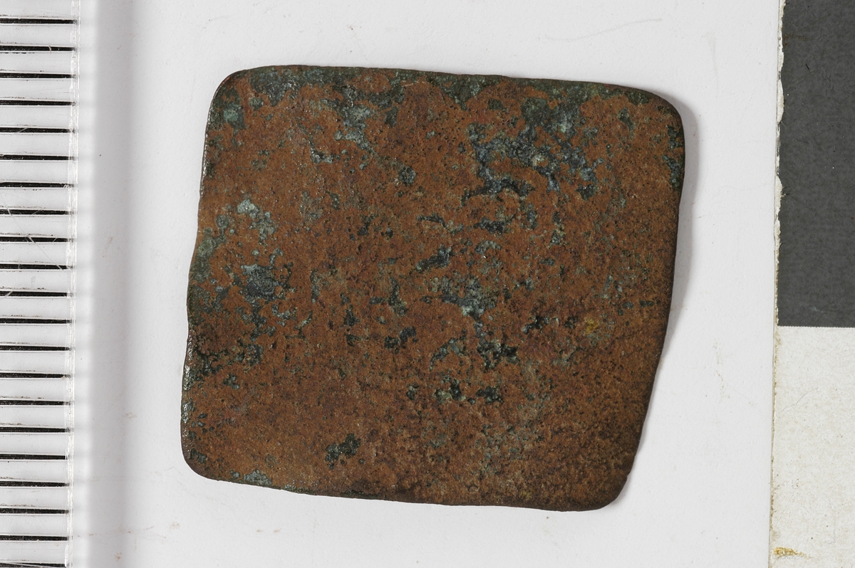 Tilnærmet firkantet plate med jevne kanter og det som kan være rester av preg. Dette kan være et vektlodd.