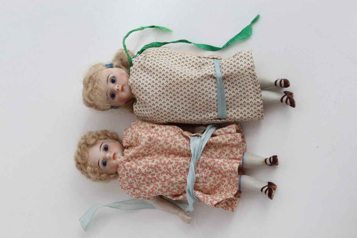 Ganske sikker giver: Karen Collett (f.1921)
To stykk små porselensdukker. Ene med kort krøllete hår, rød blomstrerte kjole med blått silkebånd og påmalt ansikt og sko. Den andre med langt lyst hår i brunprikkete kjole med blått silkebånd og påmalt ansikt og sko.