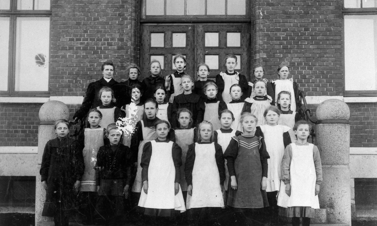 Folkskolan. Skolklass. Övre raden fr. vänster: 1. Folkskollärare Augusta Hallenius, 7. Ingeborg Johansson, 8. Harriet Fredriksson f. Bohlin. 2:a raden: 1. Ellen Jonsson, Wetterlinsgården, 4. Elsa Noring, slöjdlärare, 5. Ruth Andersson, bagare. 3:e raden: 4. Anna Eriksson (Norders Bokhandel), 5. Lilly Wennberg. 4:e raden = främre raden: 1. Märta Borg, 2. Ester Hjertman, 3. Elna Johansson, 4. Linnea Spångberg, 5. Jenny Leijon, 6. Elvira Sand.