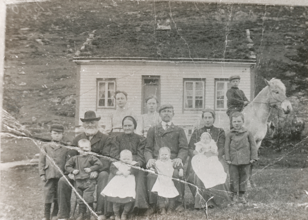 Gruppeportrett av en ukjent familie foran et hus. En gutt sitter på en hest.