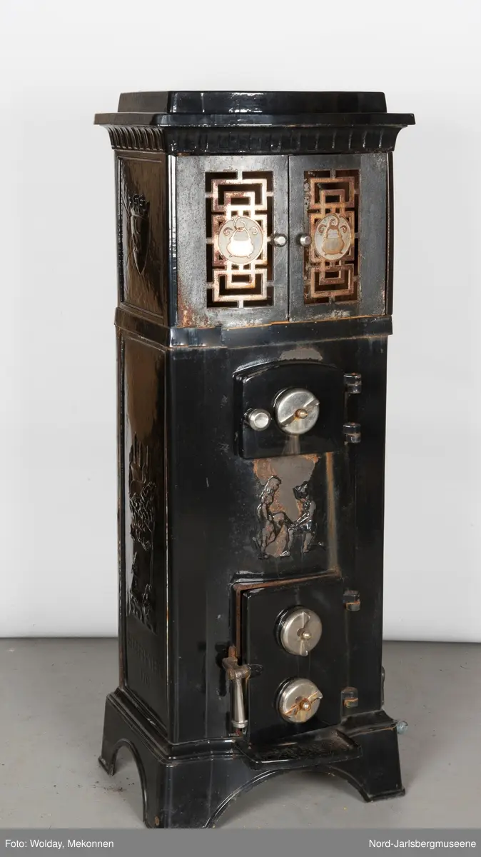 Relieffer: 1. på fronten: Askepott og prinsen som prøver om skoen passer. 2. På sidene: Askepott i grua med slottet i bakgrunnen. På grindene på dobbeltdørene til kokerom: en medaljong med grytemotiv, grinden med gjennombrutt labyrintmønster.