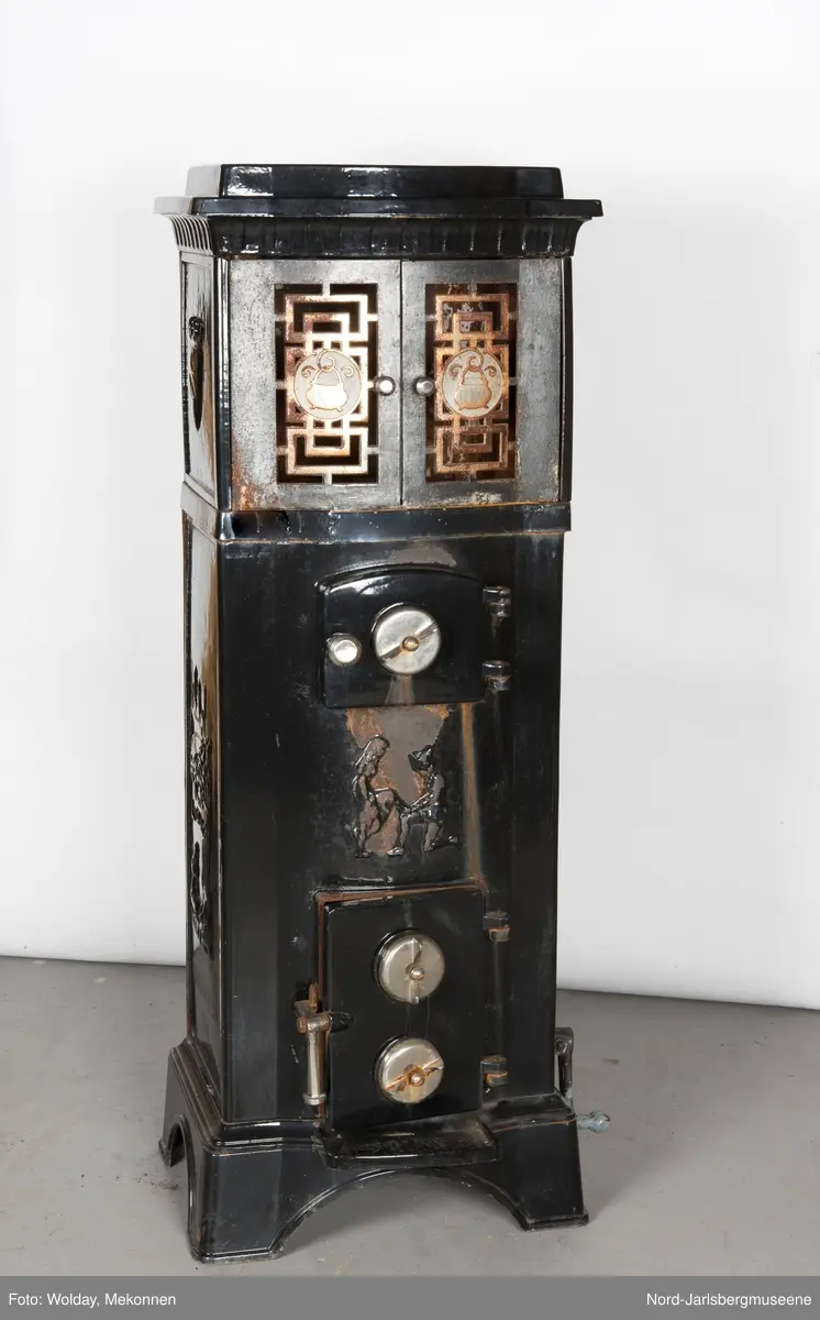 Relieffer: 1. på fronten: Askepott og prinsen som prøver om skoen passer. 2. På sidene: Askepott i grua med slottet i bakgrunnen. På grindene på dobbeltdørene til kokerom: en medaljong med grytemotiv, grinden med gjennombrutt labyrintmønster.