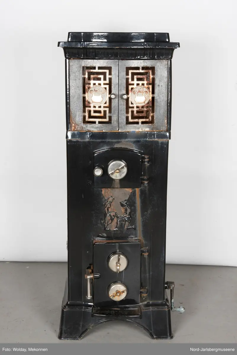 Relieffer: 1. på fronten: Askepott og prinsen som prøver om skoen passer. 2. På sidene: Askepott i grua med slottet i bakgrunnen. På grindene på dobbeltdørene til kokerom: en medaljong med grytemotiv, grinden med gjennombrutt labyrintmønster.