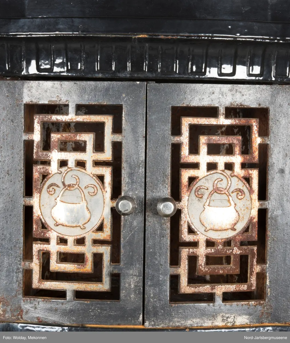 Relieffer: 1. på fronten: Askepott og prinsen som prøver om skoen passer. 2. På sidene: Askepott i grua med slottet i bakgrunnen. På grindene på dobbeltdørene til kokerom: en medaljong med grytemotiv, grinden med gjennombrutt labyrintmønster.