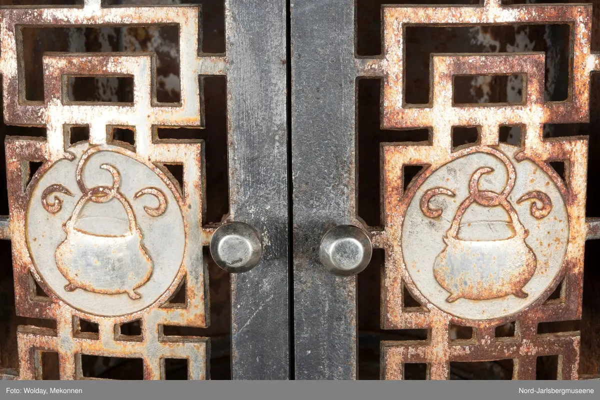 Relieffer: 1. på fronten: Askepott og prinsen som prøver om skoen passer. 2. På sidene: Askepott i grua med slottet i bakgrunnen. På grindene på dobbeltdørene til kokerom: en medaljong med grytemotiv, grinden med gjennombrutt labyrintmønster.