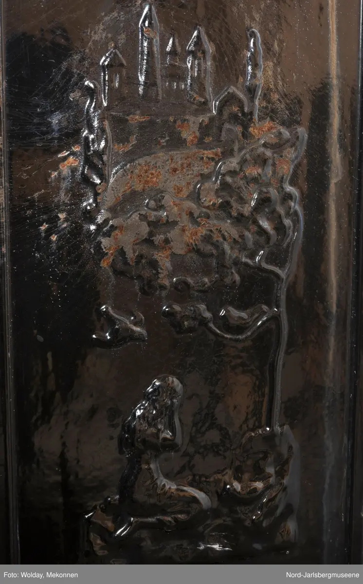 Relieffer: 1. på fronten: Askepott og prinsen som prøver om skoen passer. 2. På sidene: Askepott i grua med slottet i bakgrunnen. På grindene på dobbeltdørene til kokerom: en medaljong med grytemotiv, grinden med gjennombrutt labyrintmønster.