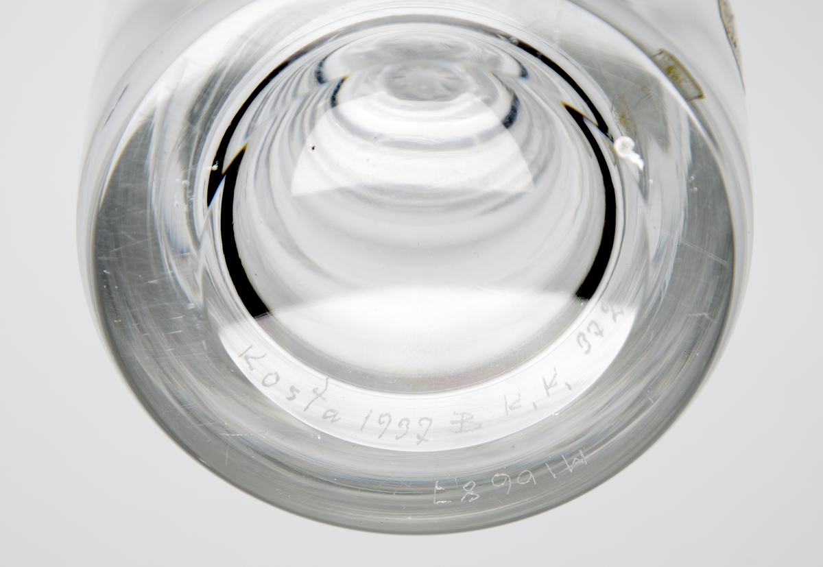 Karaff formgiven av Elis Bergh.
Se även snapsglas M 15159:a-f.
Ringoptik.
Halsen slipad i åtta facetter. Graverad fisk. Slipad propp. 
Ofärgat klarglas.
Ovan angivna mått avser höjd med propp.
Inskriven i huvudkatalogen 1959.
Funktion: Karaff