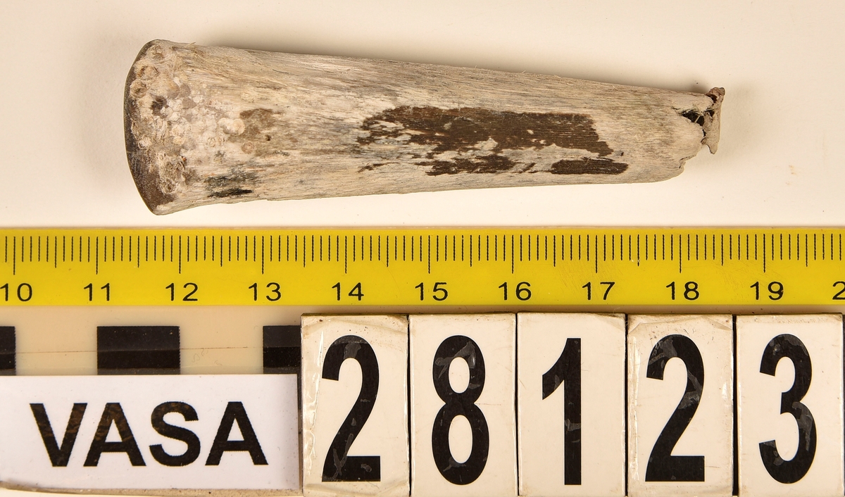 Fragment av horn. Avbruten i ena änden och sågad diagonalt till en spets i den andra änden. Ena sågytan har slipad sida. Hornets ursprungliga yta är bortnött och ytan känns närmast som torkat trä.