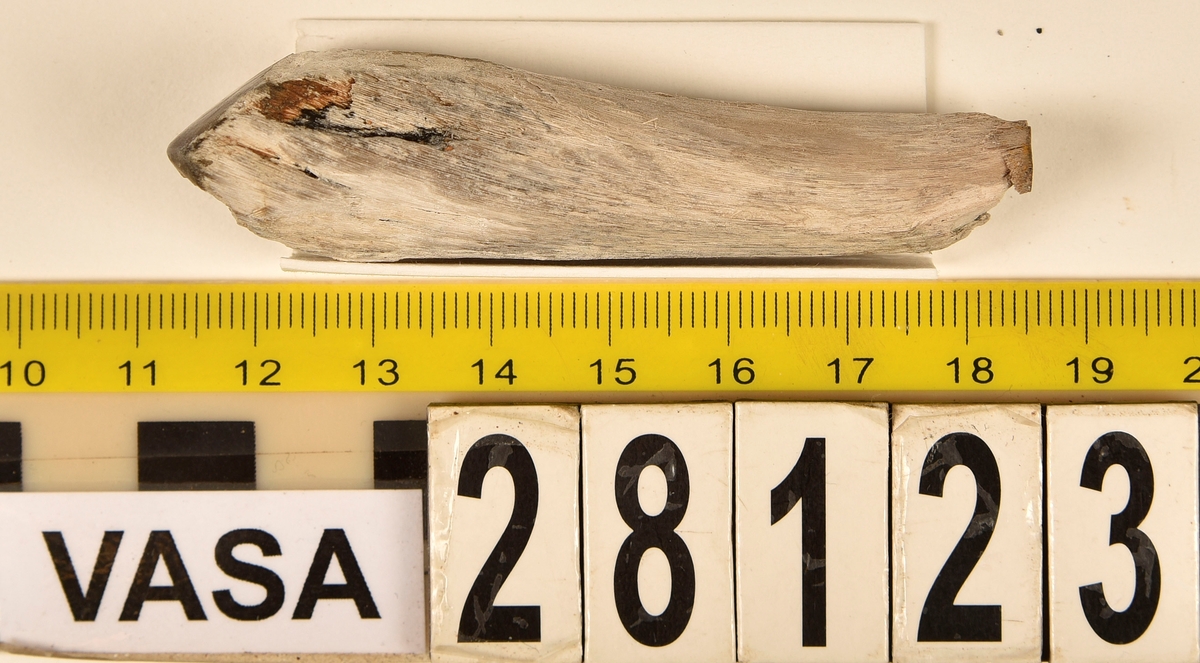 Fragment av horn. Avbruten i ena änden och sågad diagonalt till en spets i den andra änden. Ena sågytan har slipad sida. Hornets ursprungliga yta är bortnött och ytan känns närmast som torkat trä.