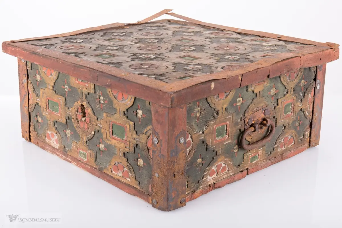 Skårede røde blomster med sirkulær innramming og grønne kvadrater med kvadratisk innramming som går i hverandre og går igjen på lokket. Innemellom disse figurene; små seksbladede hvite blomster med rød knapp. På sidene; grønne rektangler med innramming som går over i de samme røde blomstene med ramme som på lokket, men de fleste grenser mot kantene og blir halvmåneformede.