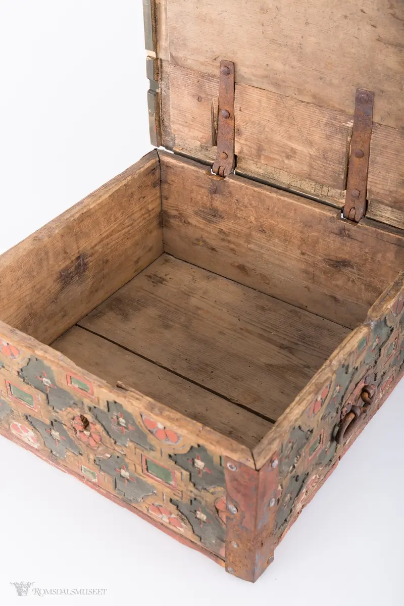 Skårede røde blomster med sirkulær innramming og grønne kvadrater med kvadratisk innramming som går i hverandre og går igjen på lokket. Innemellom disse figurene; små seksbladede hvite blomster med rød knapp. På sidene; grønne rektangler med innramming som går over i de samme røde blomstene med ramme som på lokket, men de fleste grenser mot kantene og blir halvmåneformede.