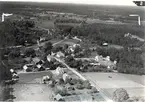 Flygfoto över Tuna. Samhället med järnvägen bostäder och skog, åkrar.