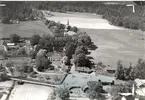 Flygfoto över Tuna. Samhället med herrgård kyrka och åkrar samt skog.