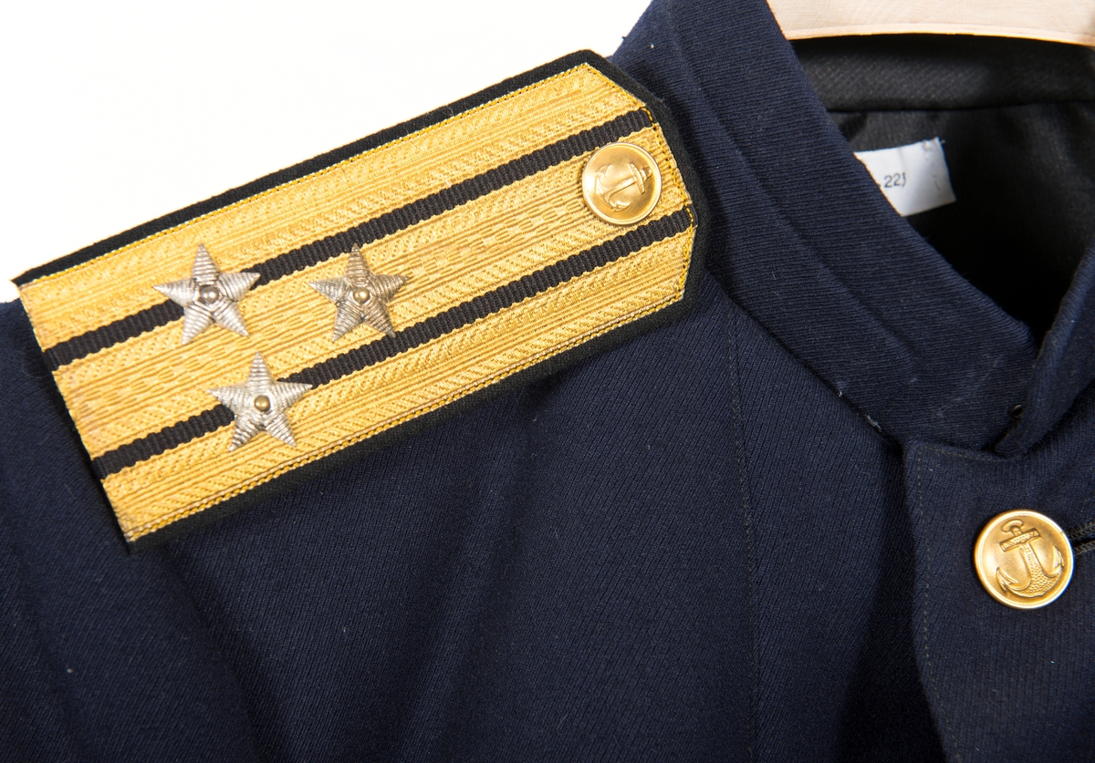 Kolett från ryska marinen för kapten av första rangen. Blått kläde. Fodrad med svart siden, i ärmarna vitt siden. Knäppt med 5 gulmetallknappar. 2 bröstfickor med lock och 2 höftfickor med lock. 1 ficka på var sida i fodret. 2 gulmetallknappar på var ärm. 1 guldstickat sterck och 1 guldstickad stjärna på var ärm. Axelklaffar med 3 längsgående guldgaloner mellan dessa svart silke, knapp i gulmetall 3 stjärnor i vitmetall.