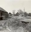 En gårdsmiljö i Ishult. Lada med spåntak till vänster, bostadshus i bakgrunden och en metervedsstapel till höger.