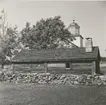 Ryggåsstuga i Stenåsa. Kyrkan syns i bakgrunden.