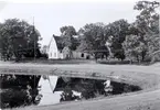 Bild av Vissefjärda kyrka, sedd från Kyrksjön. Till vänster om kyrkan kan man skönja klockstapeln.