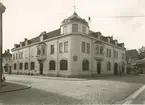 Madesjö - Örsjö Sparbank.

Bilden är tagen från hörnet Storgatan (höger) och Nya Stationsgatan. Ingången mot Nya Stationsgatan leder in till postkontoret medan ingången mot Storgatan leder in till banken. Längst till höger i fastigheten ligger Robert Nyvalls Ur- & Guldsmedsaffär. Fastigheten byggdes åren 1906 - 1907. På bankstämma 1930 fattades beslut om utvidgning av lokalerna, dels genom tillbyggnad och ändring av den av Kungliga Poststyrelsen förhyrda lokalen mot Nya Stationsgatan, dels genom en tillbyggnad mot Storgatan, varvid den fick det utseende som framgår av Olsons foto. Byggnaden revs i oktober 1953, och ett nytt bankkomplex uppfördes där nu Föreningssparbanken har sin verksamhet. 

Foto 1940-09-15