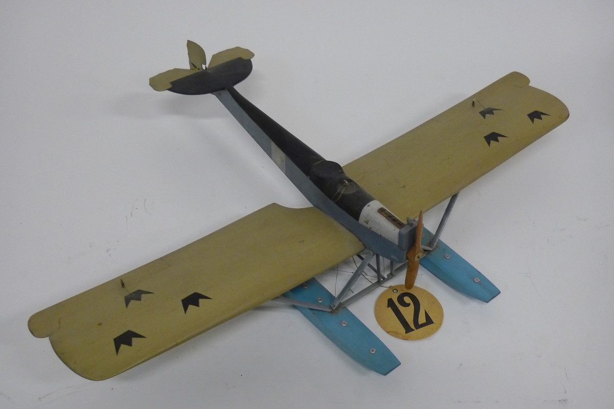 Modell av flygplan, Hansa-Brandenburg. Enmotorigt monoplan, två flottörer. Inbyggd flygkropp, placerad ovan vingarna. Breda och långa vingar med horisontala roder, vars ytterkant skjuta utanför vingarna. Stjärt med halvcirkelformad bäryta, två horisontala roder av oregelbunden form och med vågig akterkant, ett vertikalt roder. Stöttor och stag av metall. Gråmålat. Flygkropp svart- och blåmålad, flottörer blå. Motorhuv försilvrad.