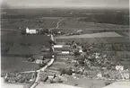 Flygfoto över Högsrum. Byn med kyrkan och ladugård samt hus och åkrar och vägen genom byn.