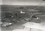 Flygfoto över Sandby. Byn med hus, ladugård, ekonomibyggnader och kyrkan samt grusvägen genom byn och åkrar.