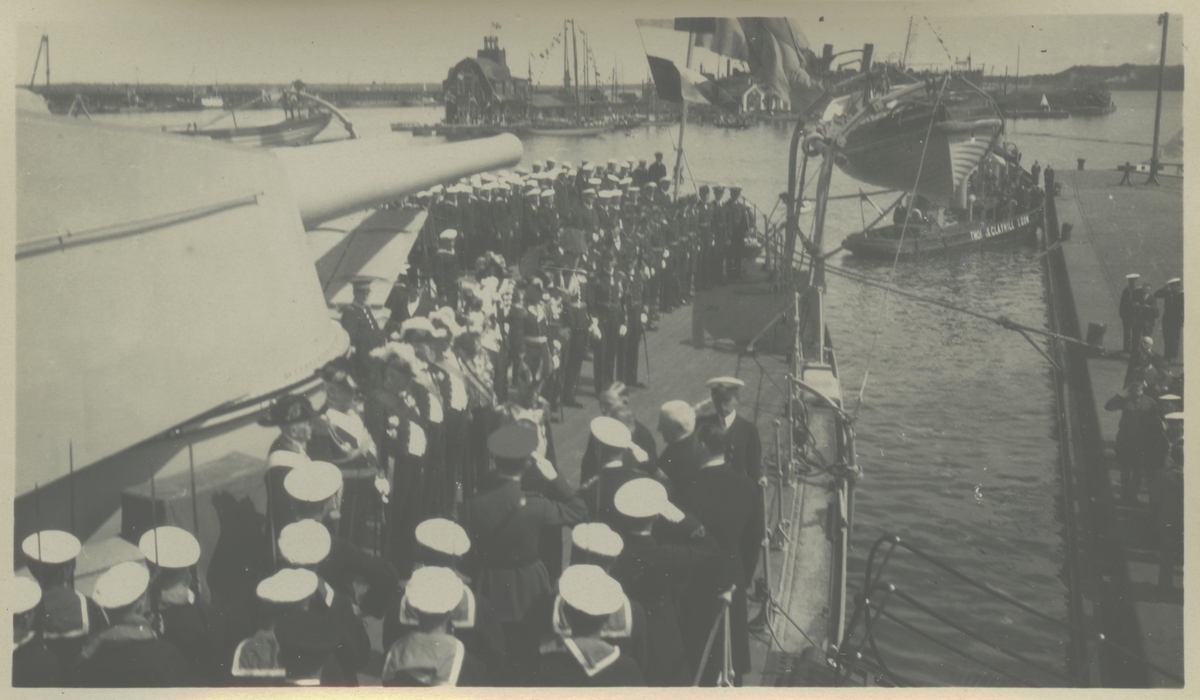 Från Gustaf V:s statsbesök i Tallinn 27-28 juni 1929. Kungen anländer på pansarskeppet SVERIGE och hälsas på däck av estniska representanter. I bakgrunden bogserbåten TUTTI från estniska handelshuset Thomas Clayhill & Son.