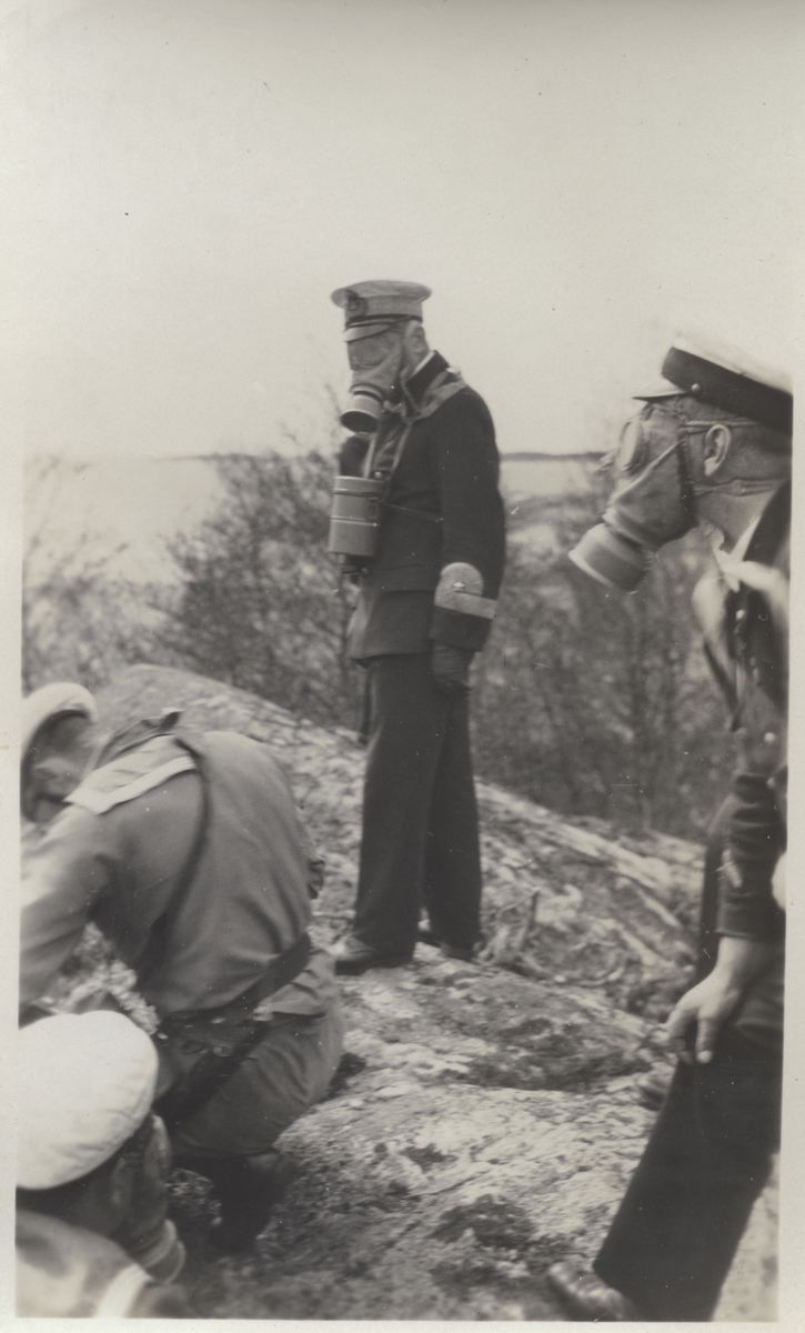 Officerare och manskap under stridsövning med gasmask. Andra bilder i Bergers samling tyder på att detta fotografi tagits vid landstigningsövningen på Stabbo i Stockholms södra skärgård 1929.