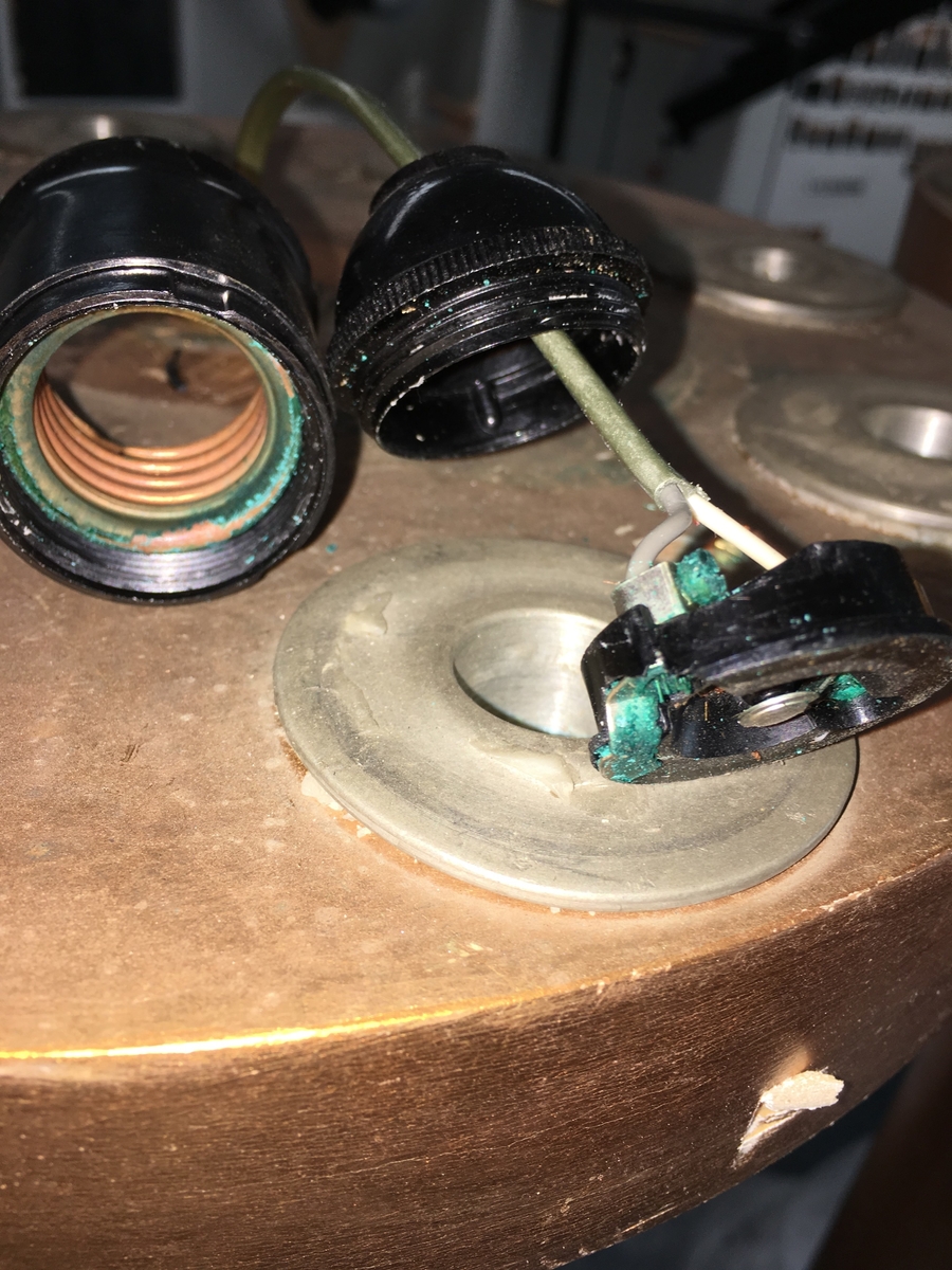 Forgylte gulvstående lamper for flere lys, både stearinlys og elektrisk. Hull til stearinlys langs kanten på hele topp-platen. En åpen lampeskjerm i glass omkranser det elektriske lyset midt på abakus, med bølgende kant (som en fakkel). Lampen er formet som en frittstående gresk søyle med base. Glatt utforming, med et område med bladutskjæringer like under midten, samt på kapitélet. Rund abakus og firkantet base. 
To av lampene har et forgylt tresylinder rundt pipen for det elektriske lyset. 
Var sannsynligvis ikke el.belysning originalt.