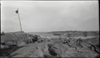 Stridsövning på Stabbo i Stockholms södra skärgård 1929. Militärer med handeldvapen ligger på klipphällar och siktar mot fartygsvrak (skjutmål?) i bakgrunden.