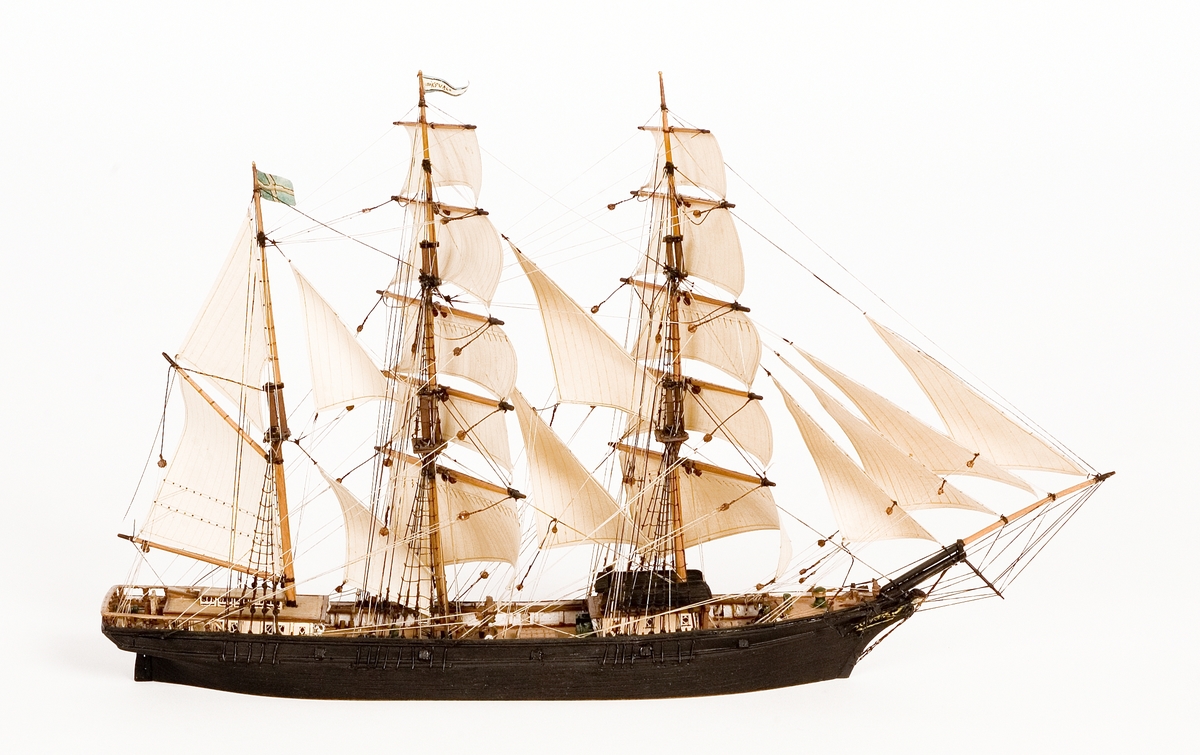 Fartygsmodell, vattenlinjemodell, hel, i block av trä, tremastade barkskeppet Hudiksvall av Hudiksvall (1864). Svartmålat skrov med galjonsbild föreställande kvinnohuvud, riggad med stående och löpande rigg, segel av papper. Två vita däckshus, två svarta livbåtar, namnvimpel på stortoppen, svensk flagga på mesantoppen.