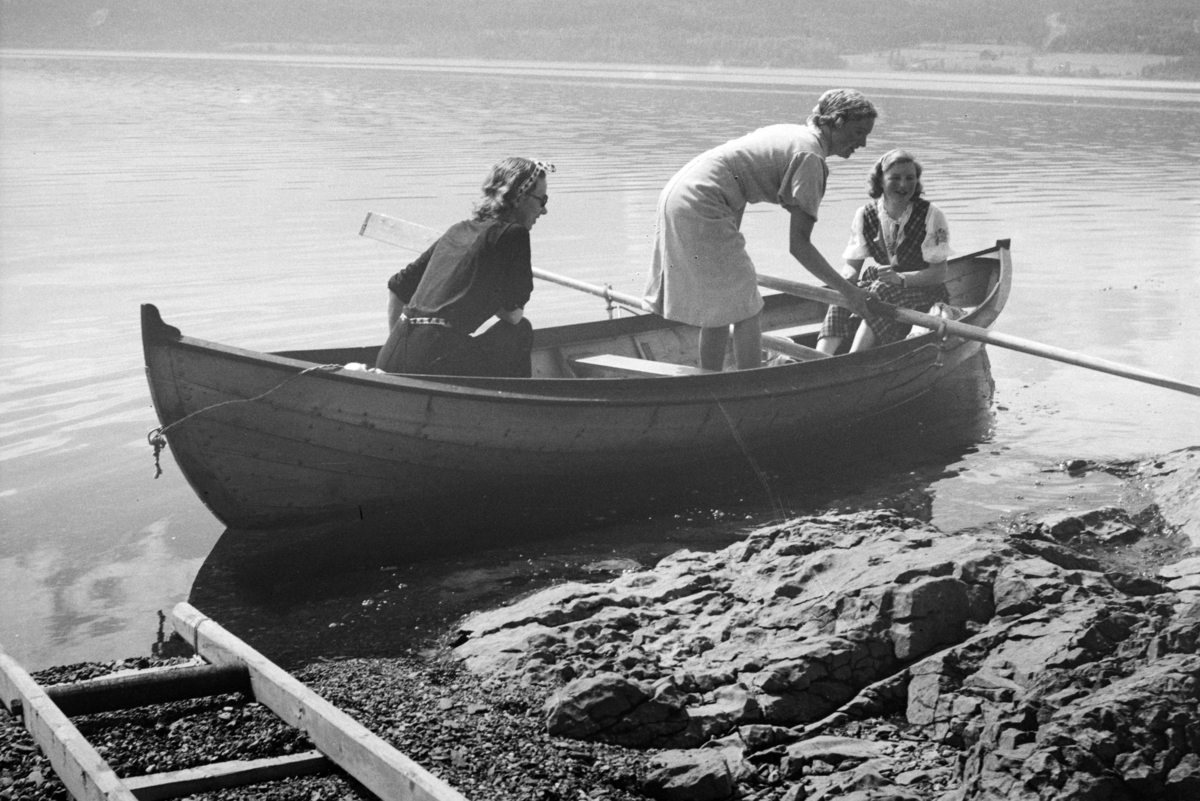 Furnes, Jessnes, Grøtodden, Hytta "Lia" til baker Johs Johannessen. Robåt (dreggebåt, mjøsbåt, Hollandbåt) Mjøsa. Til venstre sitter Lumi Johannessen. Og i midten står Ruth Oline Engebretsen (født Carlsen i 1915) Damen til høyre er Hjørdis Kristine Kjendlie (rutete kjole, født Carlsen i 1919) Ruth Oline og Hjørdis Kristine er søstre.