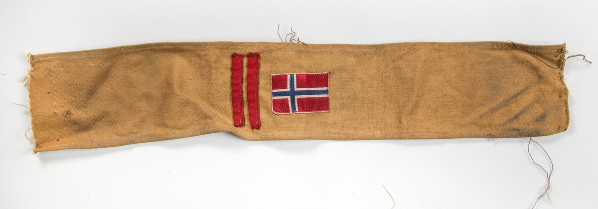 Militæruniform, Jakke (A) i grønt ulltøy. Liggane krage, stolpe i opninga med fem knappehol og fem knappar. Linning nederst med metallspenne. Ei utanpålomme på kvar side med knapp og knappehol. Skulderklaffar. Saum midt bak. Erme med mansjett, knapp og knappehol.
Bukse (B) i same tøy. Linning og gylf med knappar.  To stikklommer, to utanpåsydde lommer på framsida, og ei baklomme.
Armband (C) i gråbrunt med påsydd norsk flagg, to svarte sikkerheitsnåler (var festa til jakka).
Armband (D) i lys brunt med påsydd norsk flagg og to raude stipe (var festa til jakka).
Band (E) Smalt tjukt band (belte) med avrunda metalavslutning i endene. Spenne i eine enden og knapp i den andre.
(C D E ligg i eske i fag III, hylle 2b)