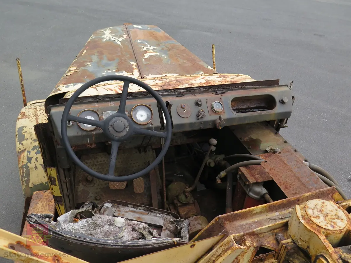 Hanomag SS 100 LN. Ombygd 2 - akslet (4 hjul) maskin med både hydraulisk gravemaskin og lasteskuffe. Gul er hovedfarge (antatt grå originalt). Fra fabrikken ble typen SS 100 LN utstyrt men en vannavkjølt 6-sylindret dieseldrevet motor av typen Hanomag D85S som yter 100 Hk ved 1500 omdreininger. Motorvolum er 8,553 liter. Motornummeret skal være 60386 om motoren er den originale. Maskinens produksjonsnummer er 432528. Girkassen er av typen ZF KB60 med 4 gir framover og ett bakover, pluss overdrive. Topphastighet 65 km/t. Det elektriske anlegget er 24 V. 20 tommers hjul, opprinnelig hadde den tvillinghjul bak. Dører finnes men sitter ikke på.
Har tre merker (stempel) med ørn og hakekors samt plate fra produsenten (på torpedoveggen).
"FROSS-BUSSING" merking i fronten (antatt grill fra en Fross- Bussing).
