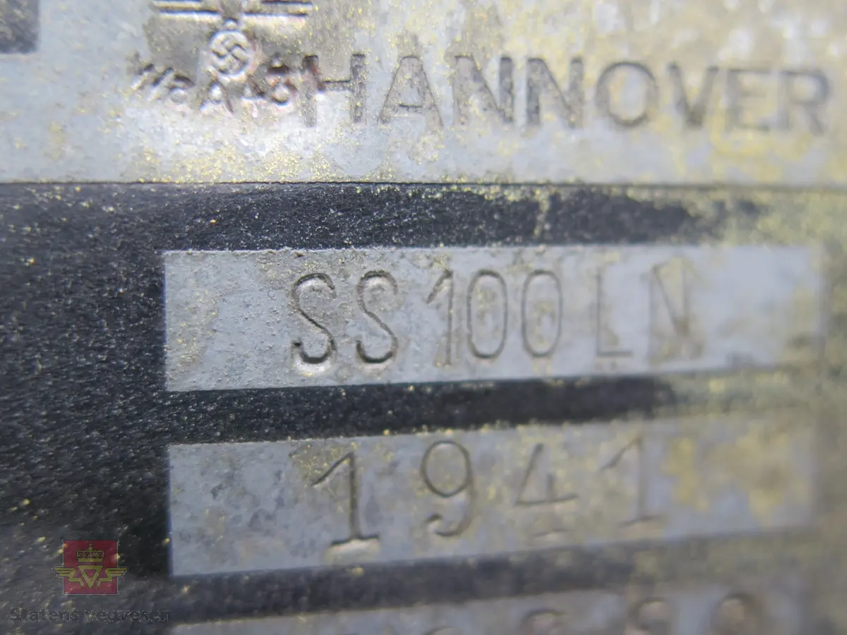 Hanomag SS 100 LN. Ombygd 2 - akslet (4 hjul) maskin med både hydraulisk gravemaskin og lasteskuffe. Gul er hovedfarge (antatt grå originalt). Fra fabrikken ble typen SS 100 LN utstyrt men en vannavkjølt 6-sylindret dieseldrevet motor av typen Hanomag D85S som yter 100 Hk ved 1500 omdreininger. Motorvolum er 8,553 liter. Motornummeret skal være 60386 om motoren er den originale. Maskinens produksjonsnummer er 432528. Girkassen er av typen ZF KB60 med 4 gir framover og ett bakover, pluss overdrive. Topphastighet 65 km/t. Det elektriske anlegget er 24 V. 20 tommers hjul, opprinnelig hadde den tvillinghjul bak. Dører finnes men sitter ikke på.
Har tre merker (stempel) med ørn og hakekors samt plate fra produsenten (på torpedoveggen).
"FROSS-BUSSING" merking i fronten (antatt grill fra en Fross- Bussing).