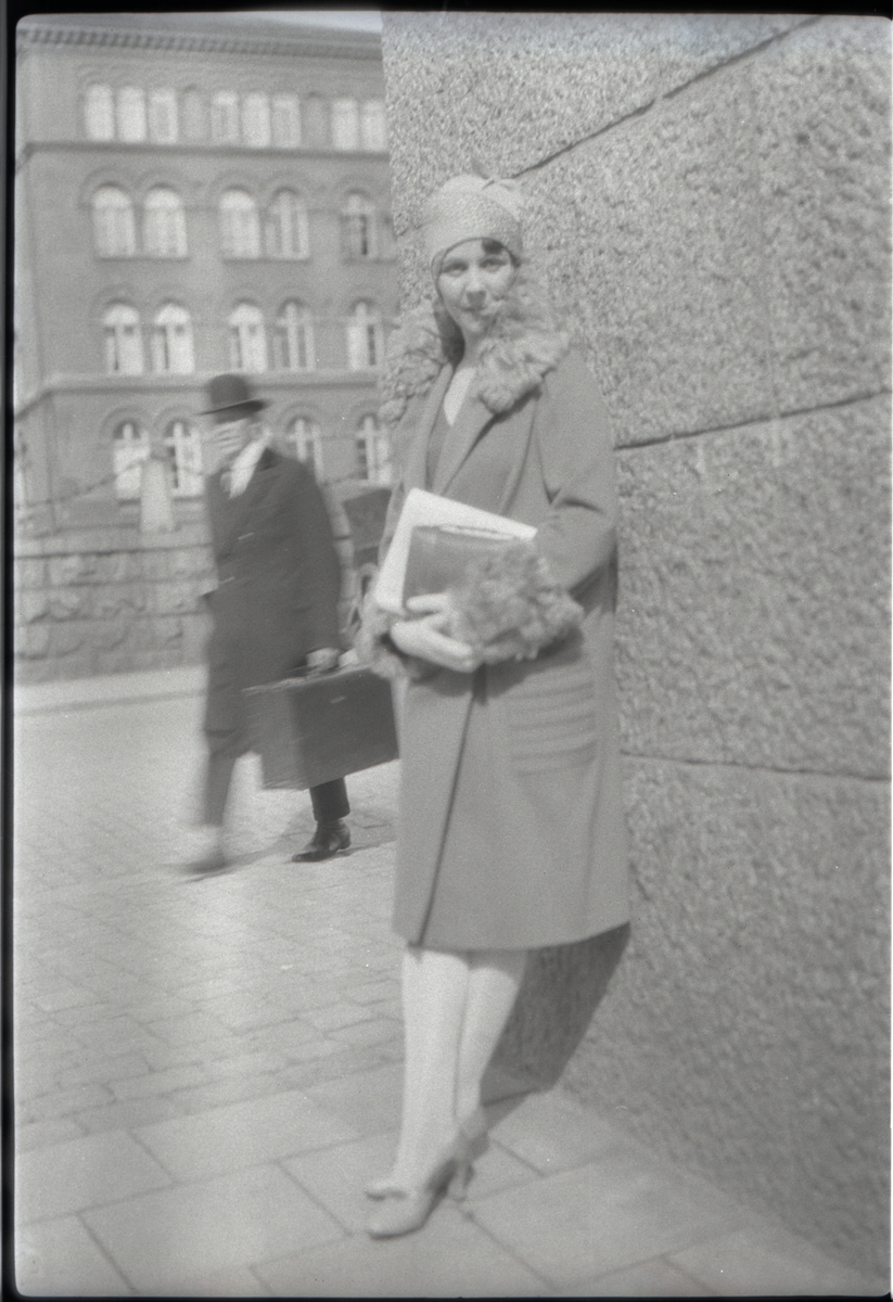 Kvinna, "E. E.", vid hörnet Linnégatan-Fredrikshovsgatan på Östermalm i Stockholm våren 1929. I bakgrunden skymtar det som tidigare var livgardesregementenas kasernbyggnader men som i dag (2017) är en del av kontorskomplexet Garnisonen.