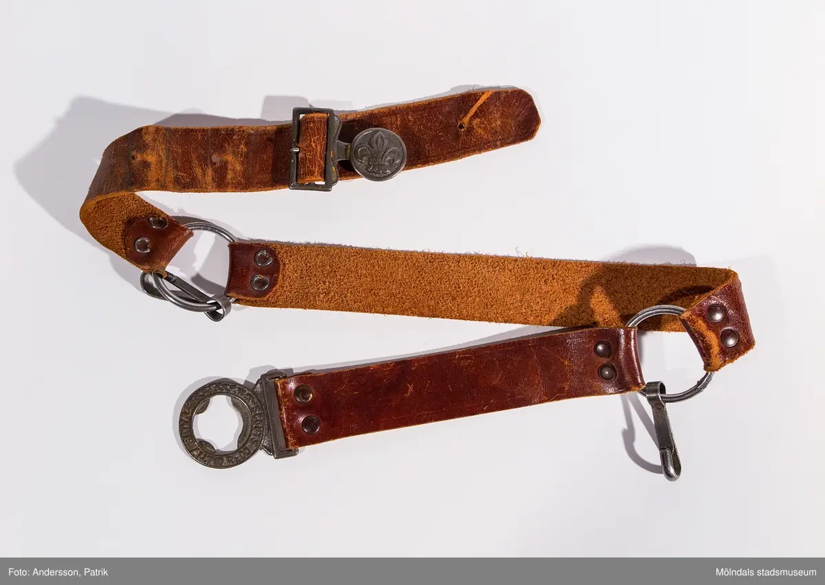 Scoutskärp i tre delar, av brunt skinn, som hålls ihop av två metallringar fastsatta med nitar samt knäppe. I ringarna hänger var sin karbinhake. Metallknäppet består dels av en scoutsymbol (fransk lilja) samt en ring med gjuten text "BOY SCOUTS ALLTID REDO". Fyra hål finns för att reglera faststängning med. Skärpet har använts av givarens broder under dennes nyingperiod från 8 till 14 års ålder.