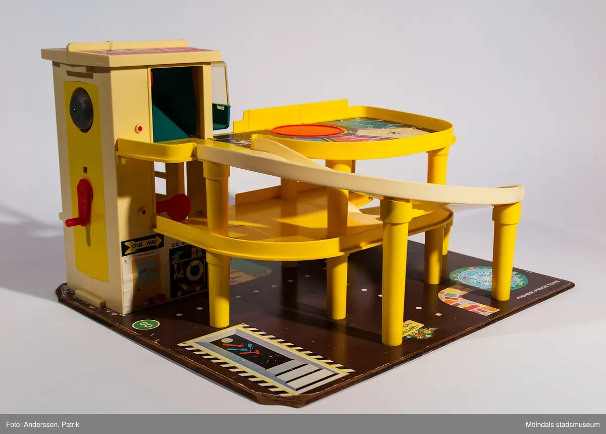 Fisher-Pricegarage från 1970-talet. Inköpt 2001 på Second Hand av givaren, vars barn har lekt med det. Garaget är i tre plan och står på en masonitplatta. Det har person-/bil-hiss med vevfunktion och pling från plan 1-3, vev att snurra vänd-platta på våning 3, tankstation på plan 1 samt två nedförsbackar från plan 2 och 3 till plan 1. Nivåskillnaderna är uppbyggda med plaststolpar vilket gör att bilar lätt åker nedför backarna.