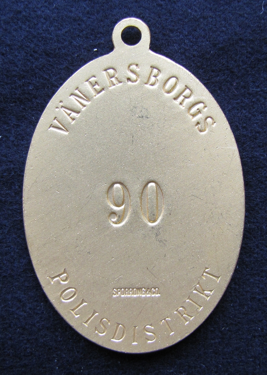 Polisbricka, oval med en ögla i toppen. 

På framsidan: Lilla riksvapnet, dvs en krönt sköld med tre kronor. Bakom skölden eklöv och korslagda fasciner. Under emblemet står det POLIS.

På frånsidan: VÄNERSBORGS POLISDISTRIKT står den i det övre och undre kanten. Mitt på står siffran 90. Även tillverkaren Sporrong & CO, Stockholm finns ingraverat.