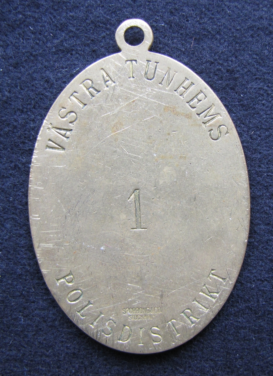 Polisbricka, oval med en ögla i toppen. 

På framsidan: Lilla riksvapnet, dvs en krönt sköld med tre kronor. Bakom skölden eklöv och korslagda fasciner. Under emblemet står det POLIS.

På frånsidan: VÄSTRA TUNHEMS POLISDISTRIKT står den i det övre och undre kantenkanten. Mitt på står siffran 1. Även tillverkaren Sporrong & CO, Stockholm finns ingraverat.