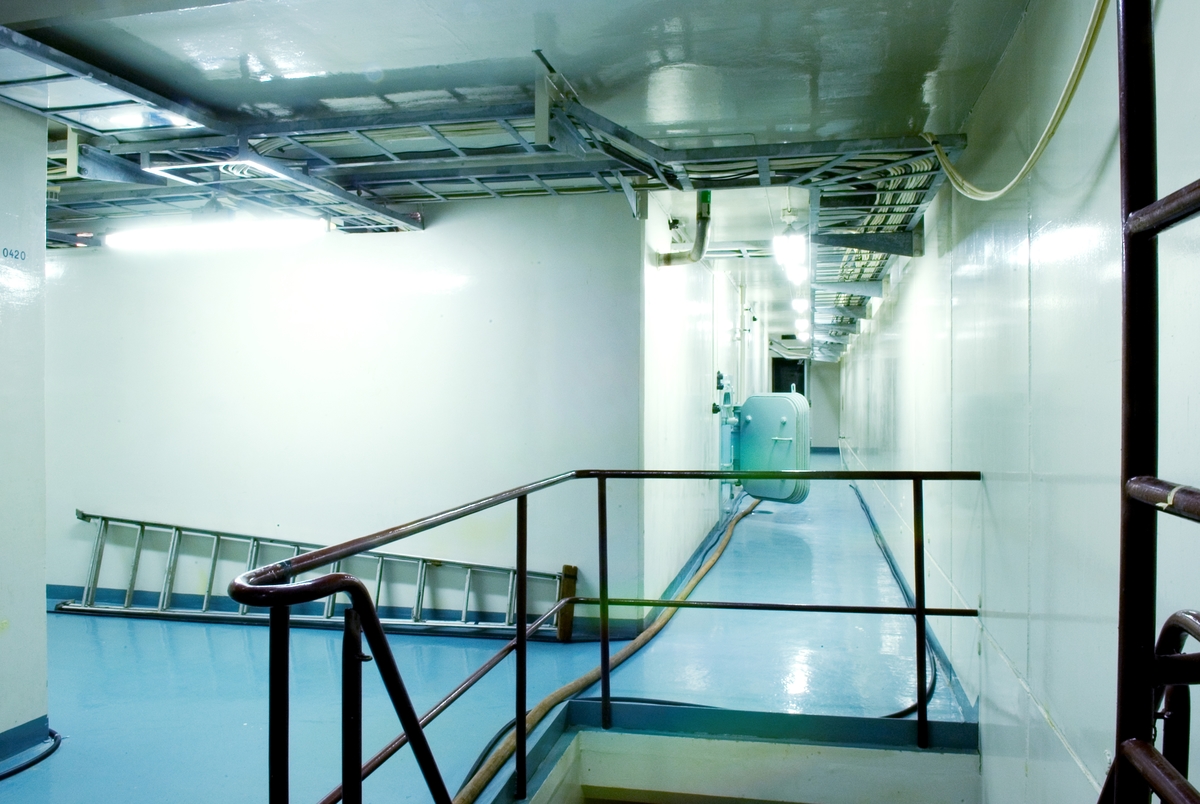 Ågesta kärnkraftverk. Under 2005 gjorde Tekniska museet tillsammans med Stockholms Läns Museum och Länsstyrelsen i Stockholms län en fotodokumentation av Ågesta kraftvärmeverk, Sveriges första kommersiella kärnkraftverk, Foto: Nisse Cronestrand. Bildbeskrivningar: Ingenjör Åke Bergman.

Bilden föreställer: Plan 04 korridor 0419. Taget från hissplan 0420 med trappa i förgrunden ned till rum 0020. Strålskyddsdörr till rum 0427 står öppen. Där innaför finns D2O pumpar i system P90 & P91 samt öppning till rum 0428 med dränagetank P91. Installlationer i 0427: P88, P90, P91, P92, P96, P200, P205, P220, P248, samt P250. Installationer i 0428: P88, P90, P92, P96, P200, P205, P248, samt P250. Förklaring av system framgår av rapport :Statens Vattenfallsverk A23/60 5/4 1960.