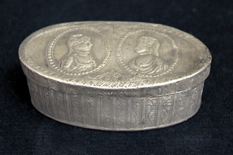 Oval snusdosa. På locket två medaljonger med kvinnobyster, sidorna och botten ornerade med omväxlande stolpar och rankor.