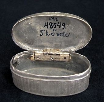 Oval snusdosa. På locket två medaljonger med kvinnobyster, sidorna och botten ornerade med omväxlande stolpar och rankor.