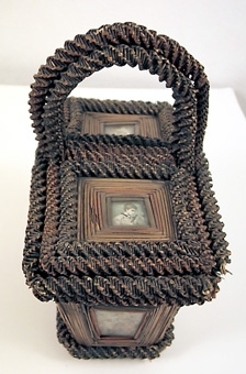 KORG, REKTANGULÄR, HANDTAG, TVÅ LOCK. ÅTTA ST INGLASADE BILDER PÅ LOCKEN OCH SIDORNA. GLAS UNDER BOTTEN. RUNT MOTIVEN FINNS STRÅN SOM I SIN TUR ÄR OMGIVNA AV RINGLANDE BUNDNA STRÅN.